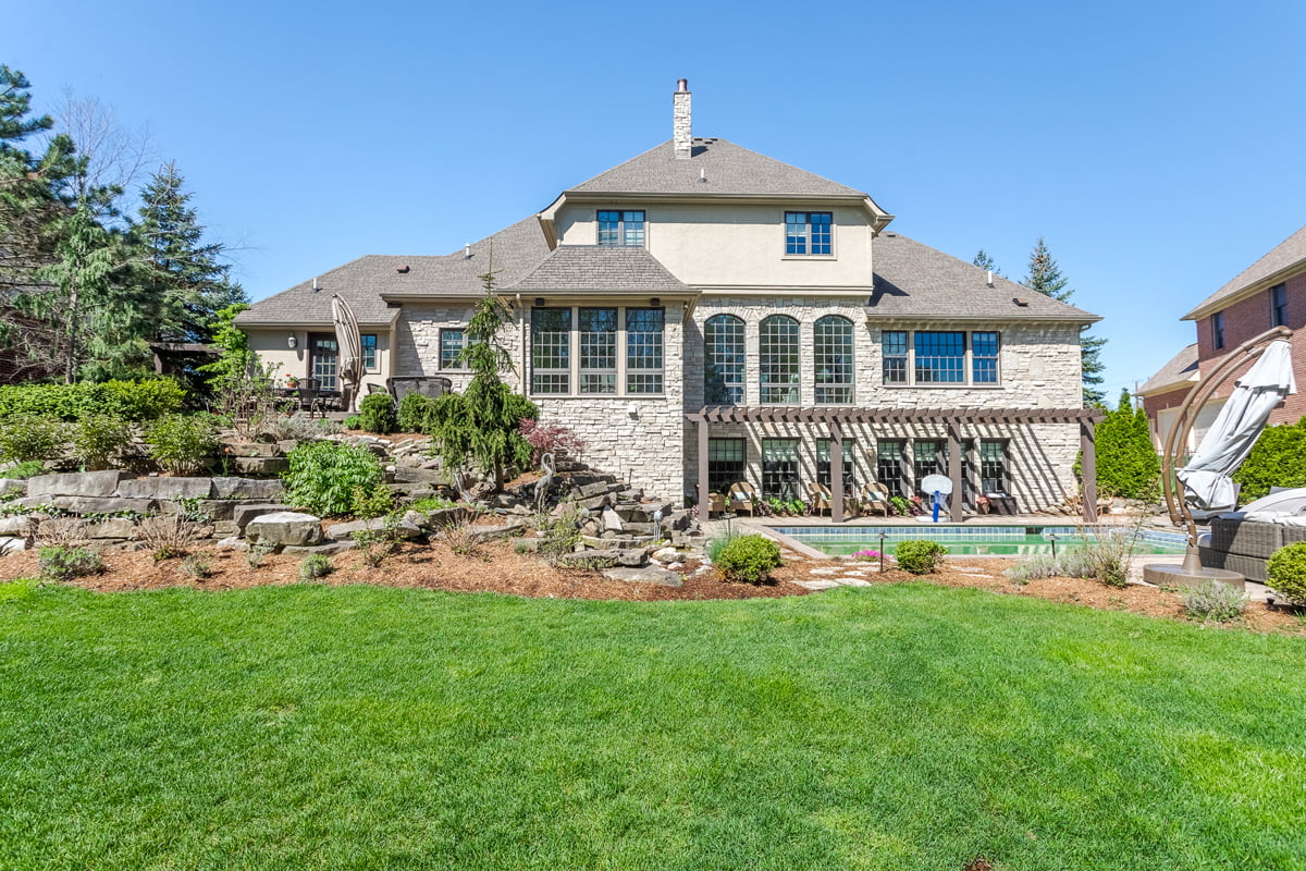 Aerial view of a high-end Farmington home showcasing its landscaped backyard, waterfall rock feature, pergola-shaded poolside area, and elegant stone exterior.