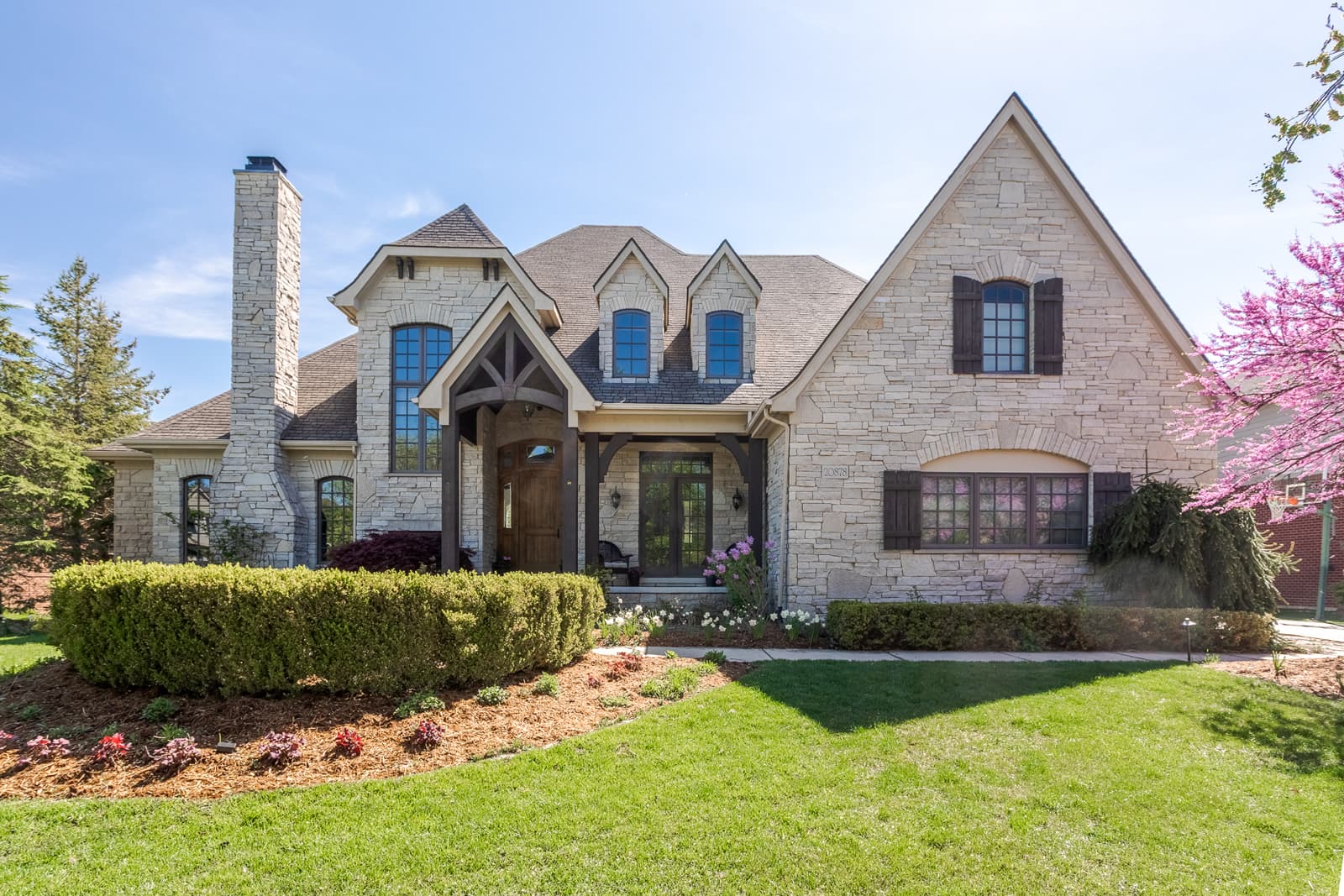 Impressive front view of a Farmington luxury home with stone façade, manicured landscaping, and charming architectural details.