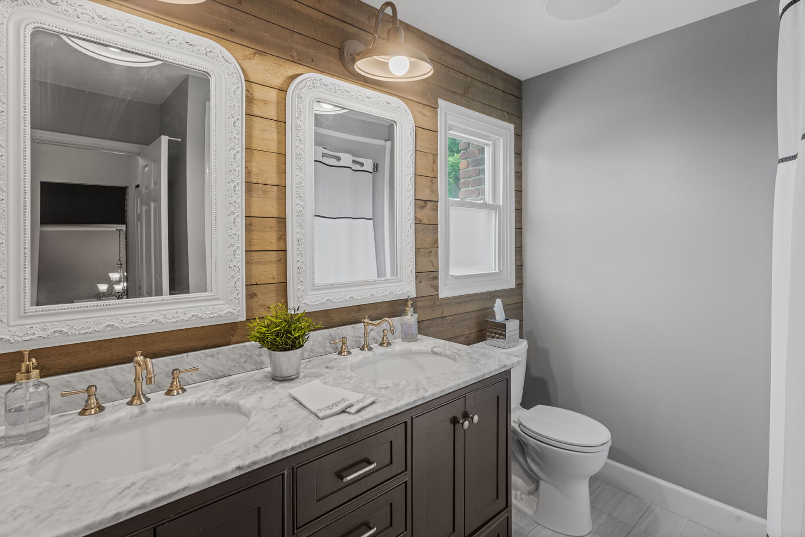Stylish Farmington bathroom featuring a marble double vanity, wood accent wall with dual framed mirrors, and soft brass fixtures for a rustic-modern touch.