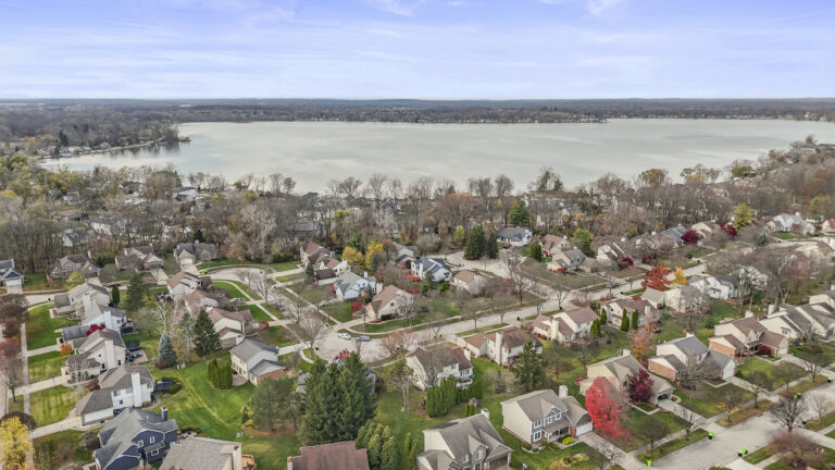 Aerial view of a residential neighborhood in Novi, MI with tree-lined streets, single-family homes, and a large lake.