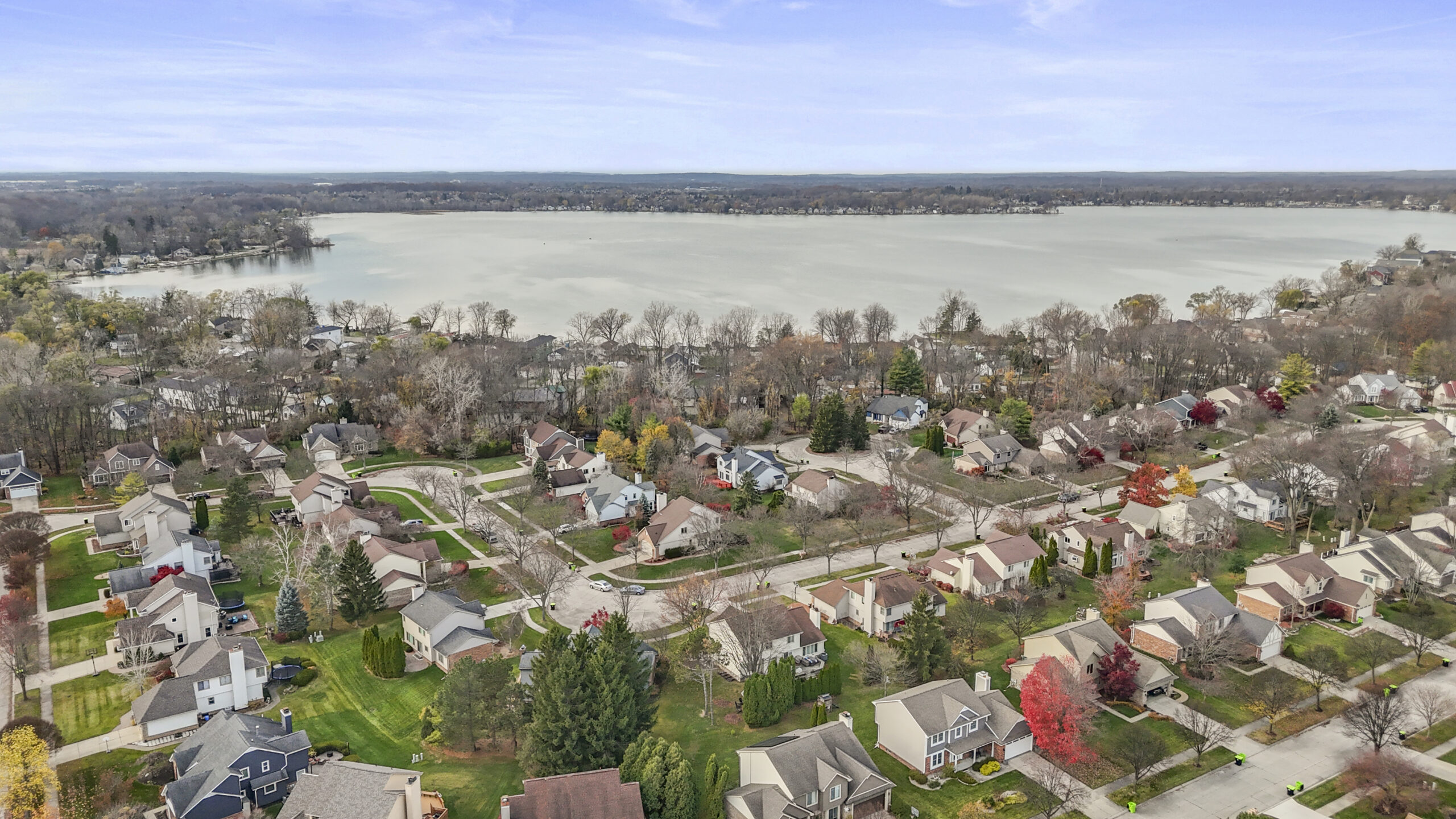 Aerial view of a residential neighborhood in Novi, MI with tree-lined streets, single-family homes, and a large lake. 