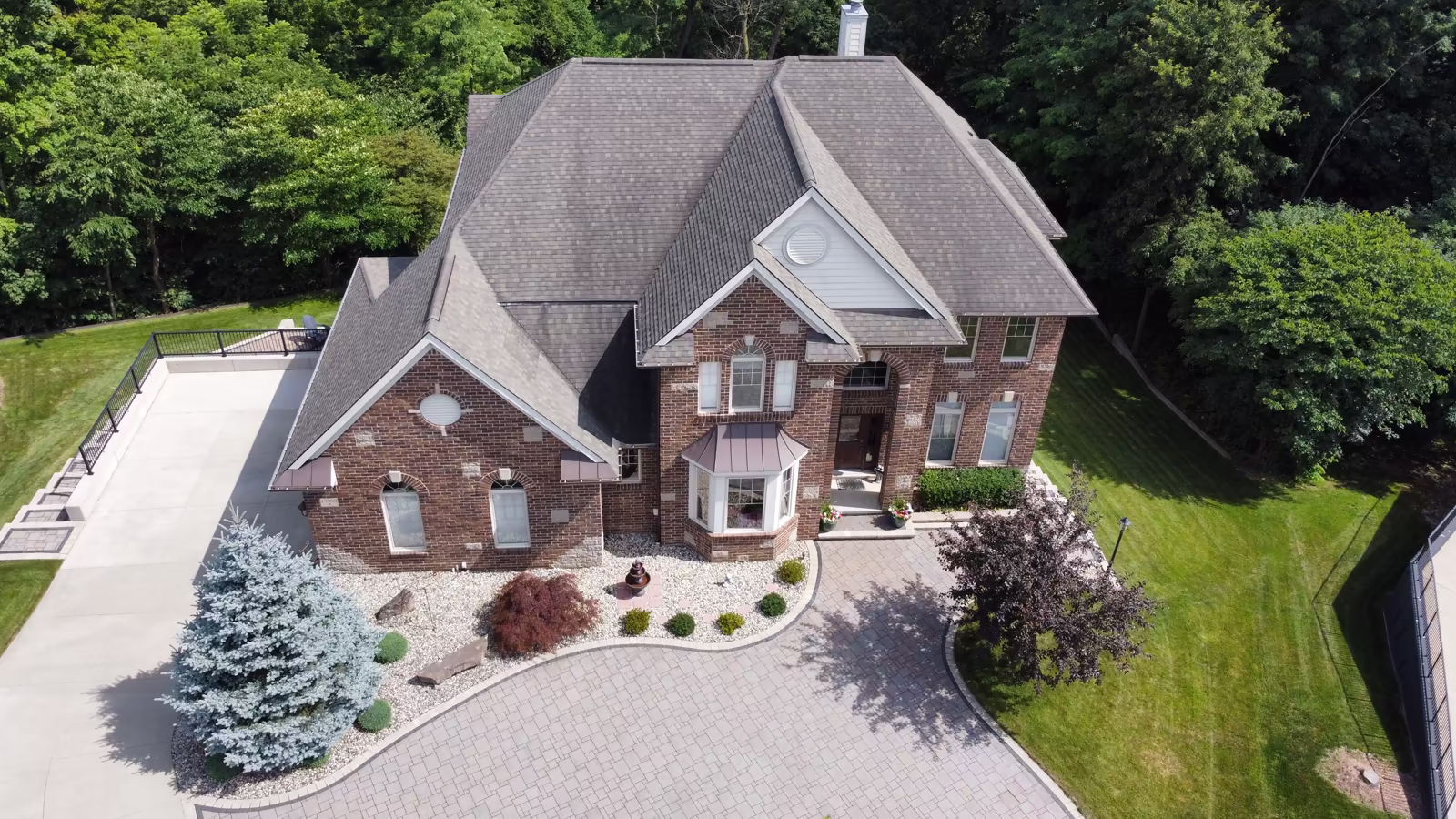 Luxury brick estate home in Northville, Michigan with circular driveway and wooded backyard aerial view.