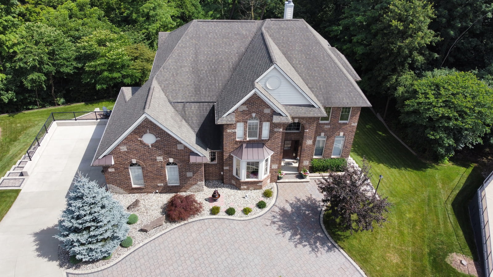 Luxury brick estate home in Northville, Michigan with circular driveway and wooded backyard aerial view.
