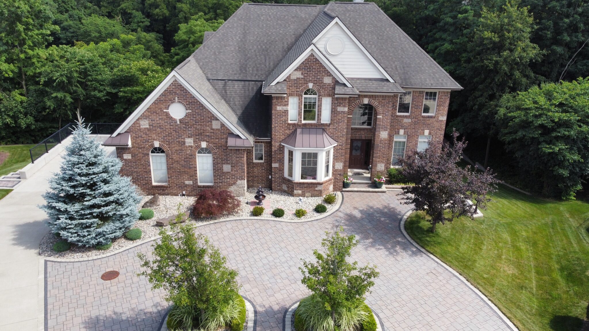 Large brick home in Northville, Michigan, with mature trees, and a large paver brick walkway.