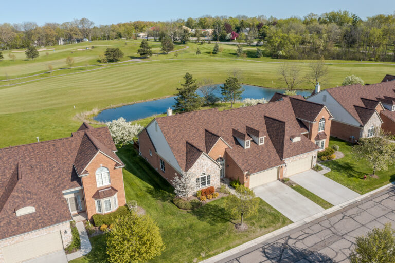 Aerial view of brick homes in Farmington, MI with landscaped yards, a pond, and expansive green space