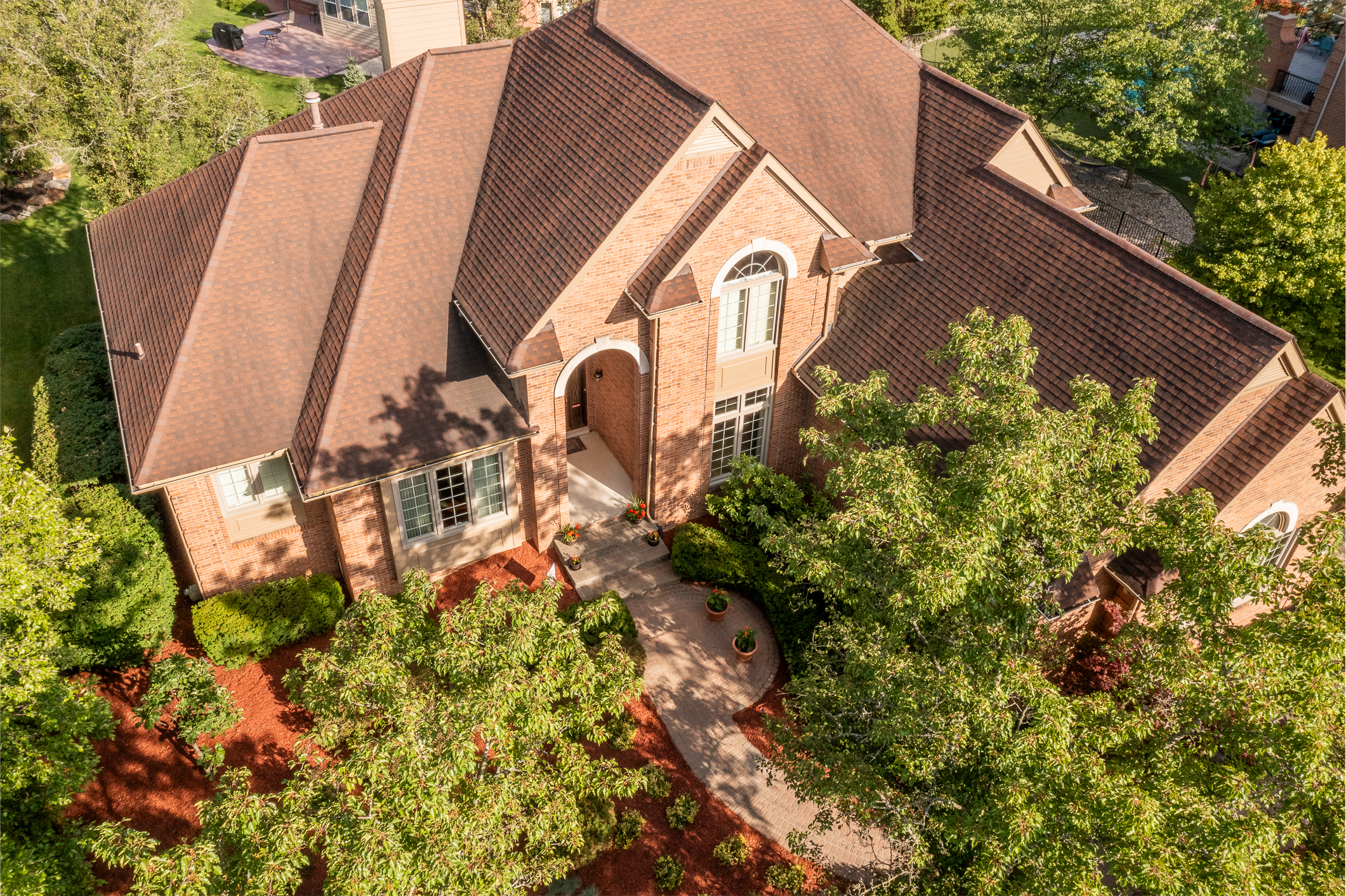 Two-story brick home in a tree-lined Novi, Michigan neighborhood with a landscaped front yard.
